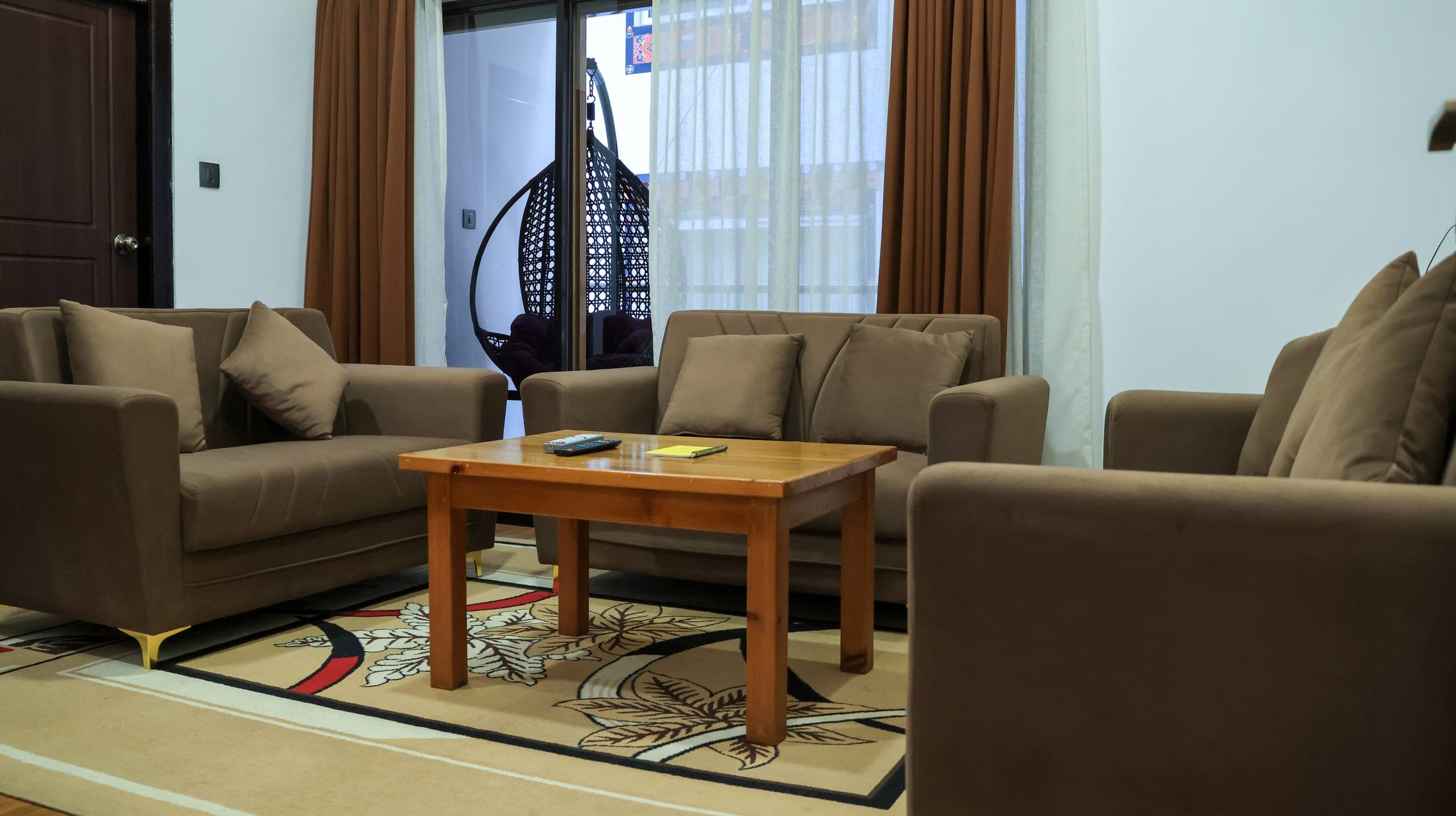 Suite sitting room with brown sofas, a wooden coffee table and a hanging chair by the veranda