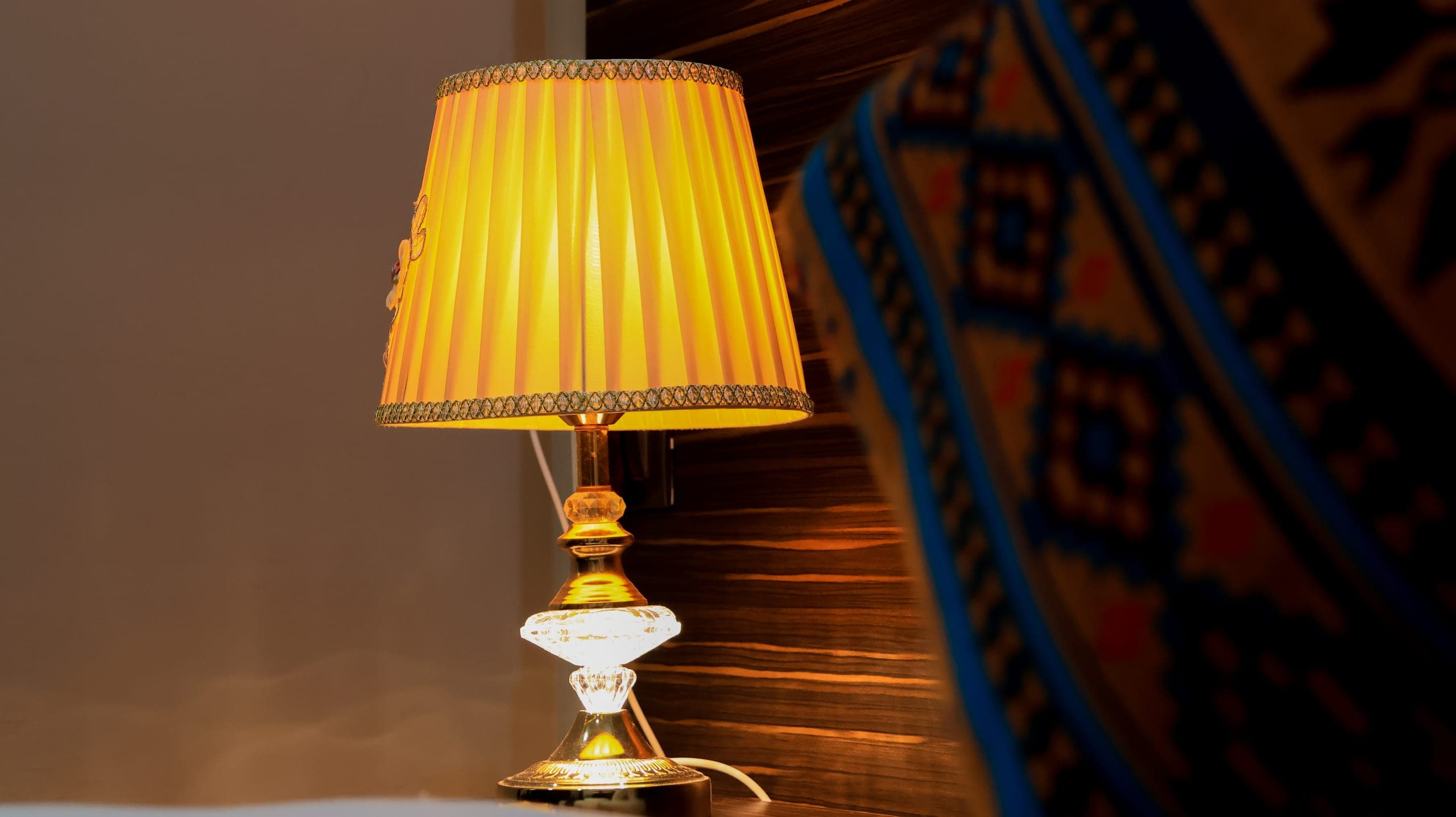 Warm bedside lamp beside a Bhutanese-patterned cushion
