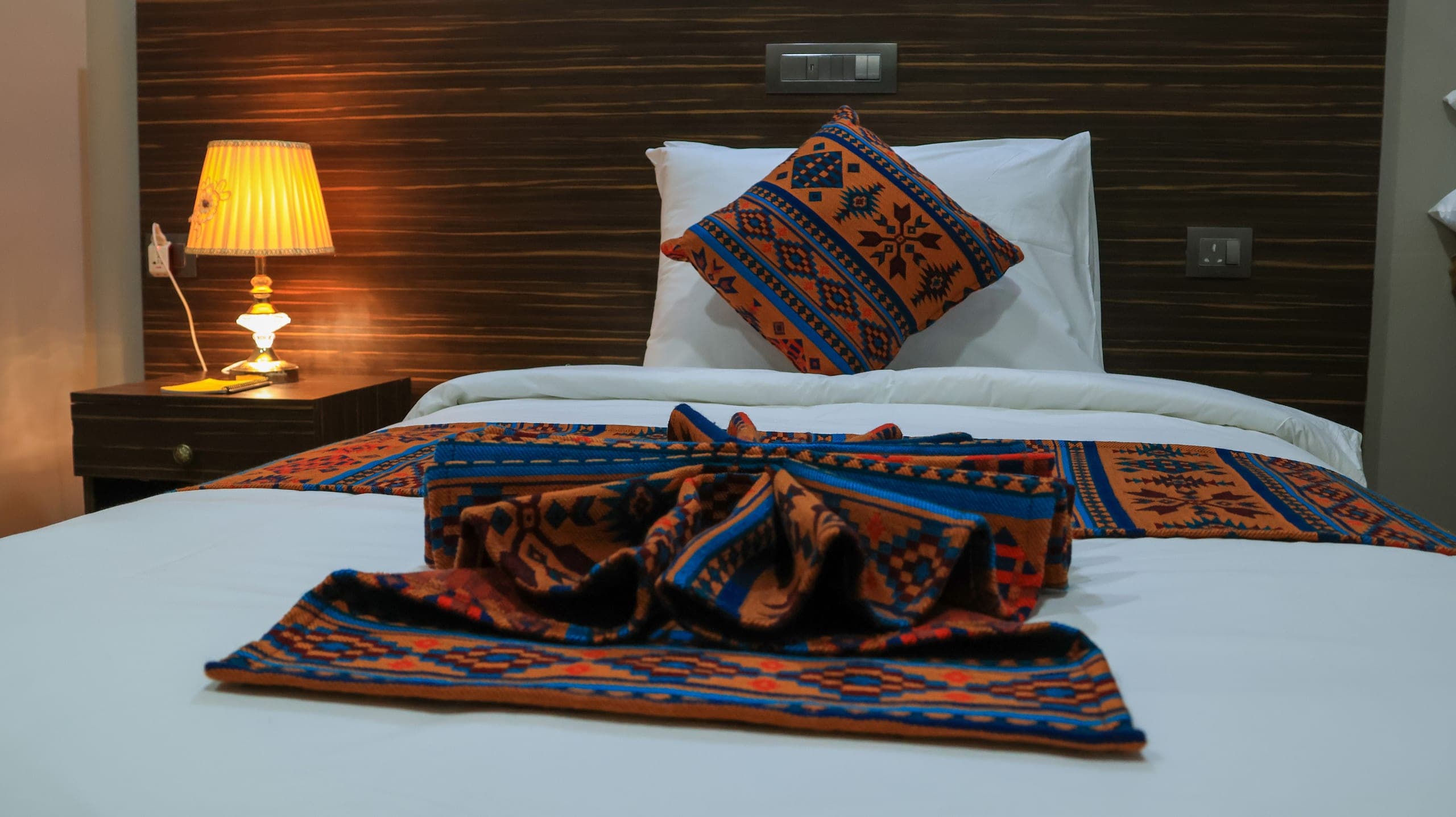 Folded Bhutanese-pattern textile and cushion on a white bed