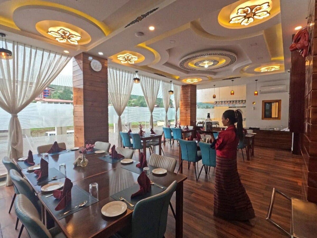 Restaurant with blue chairs, set tables and sheer curtains, with a staff member in traditional kira